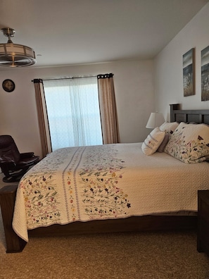 Una camera da letto con un letto, una sedia, una lampada, una ventola a soffitto e una finestra con tende.