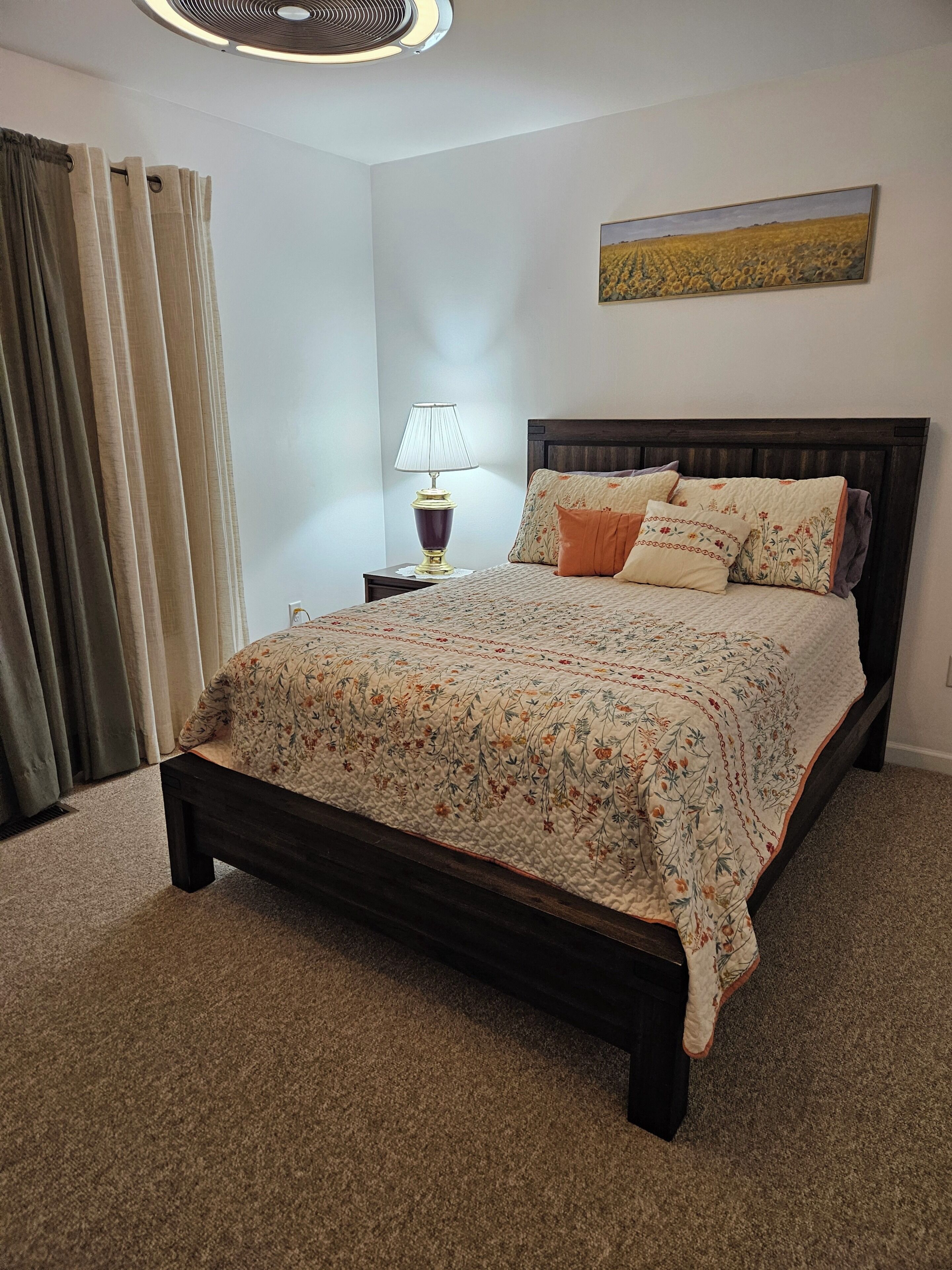 A bedroom with a bed, a nightstand, a lamp, a painting, and curtains.