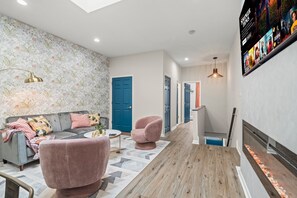 Una sala de estar moderna con un sofá, dos sillones rosados, una mesita de centro y un papel tapiz estampado.