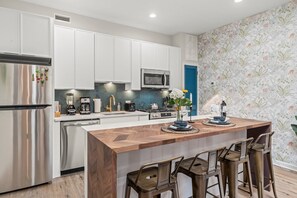 Una cocina moderna con armarios blancos, electrodomésticos de acero inoxidable, una isla de madera con taburetes altos y un salpicadero decorativo.