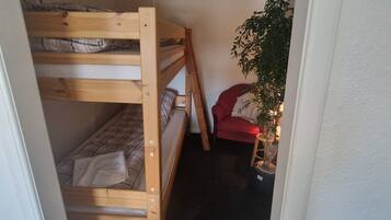 Una habitación pequeña y cerrada con una cama doble, una silla roja y una planta en maceta.