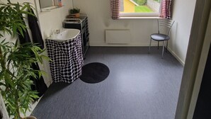 A small, compact room with a single window, a radiator, a chair, a round rug, and a potted plant. - Knudstrup Kro & Hotel (Kjellerup)