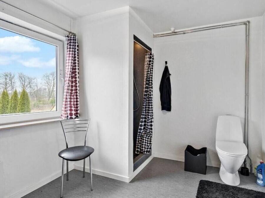 A modern bathroom with a toilet, a shower area, and a window with a view of trees.