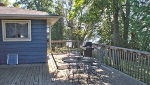 Une terrasse avec des chaises et une table en métal, un barbecue et une vue sur les arbres.