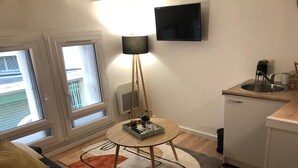 A compact living space with a kitchenette, a round table with a lamp, and a view through a window. - Independent Cozy Room (Montpellier)