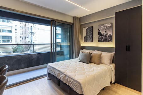 A modern bedroom with a large bed, a sliding glass door to a balcony, and artwork on the wall.