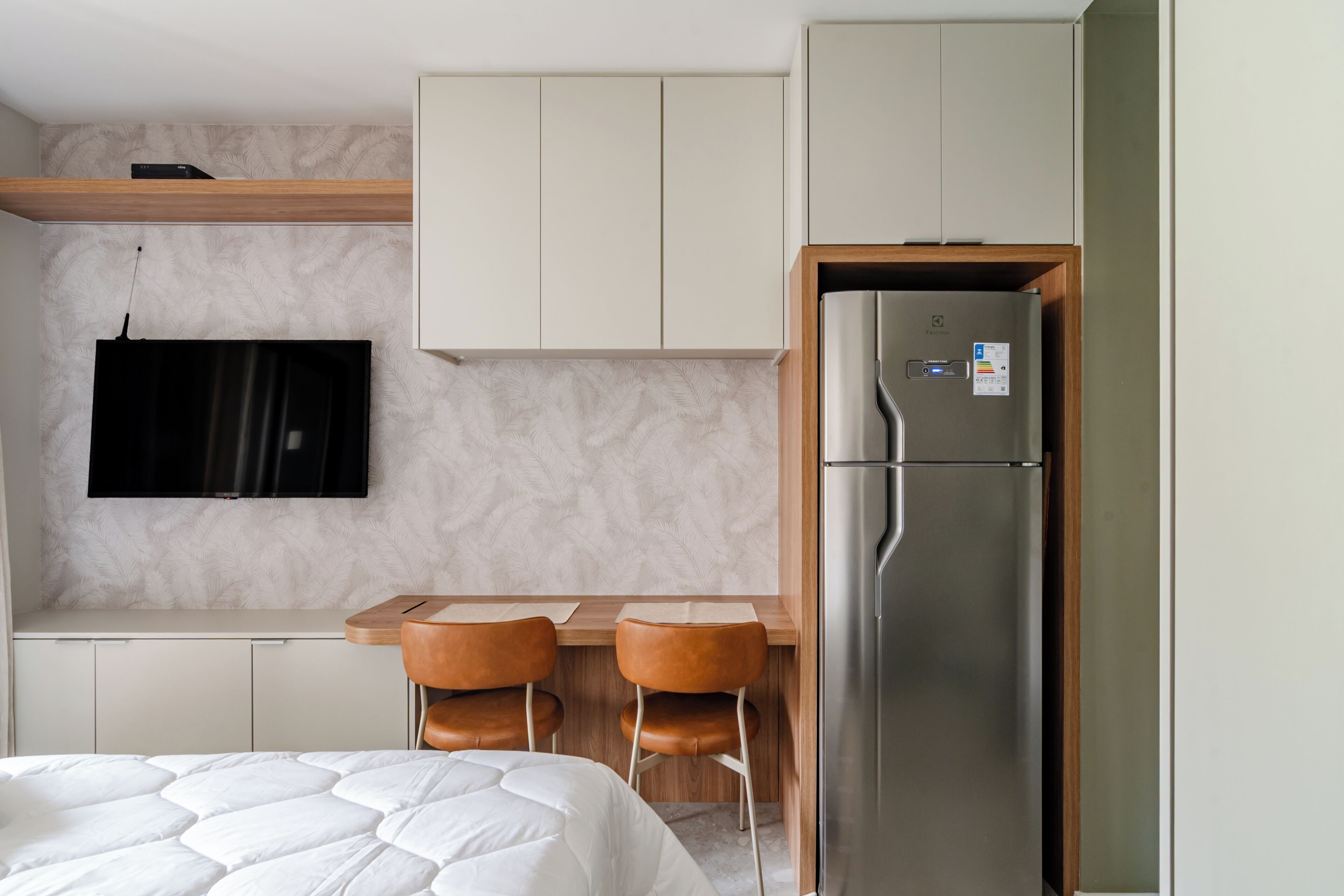 Ein modernes Hotelzimmer mit Bett, Flachbildfernseher, Holztisch mit zwei Stühlen und integriertem Kühlschrank.
