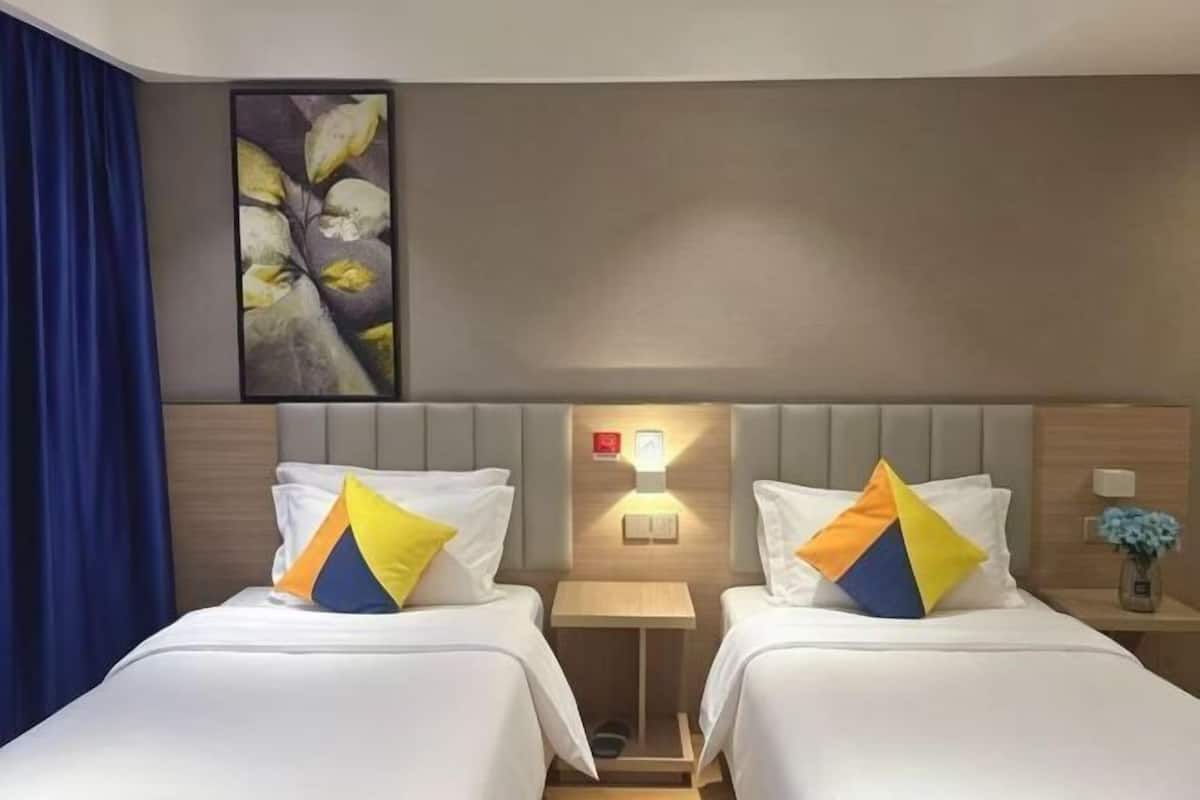 Quarto de hotel com duas camas, cabeceira com luz e uma obra de arte na parede.