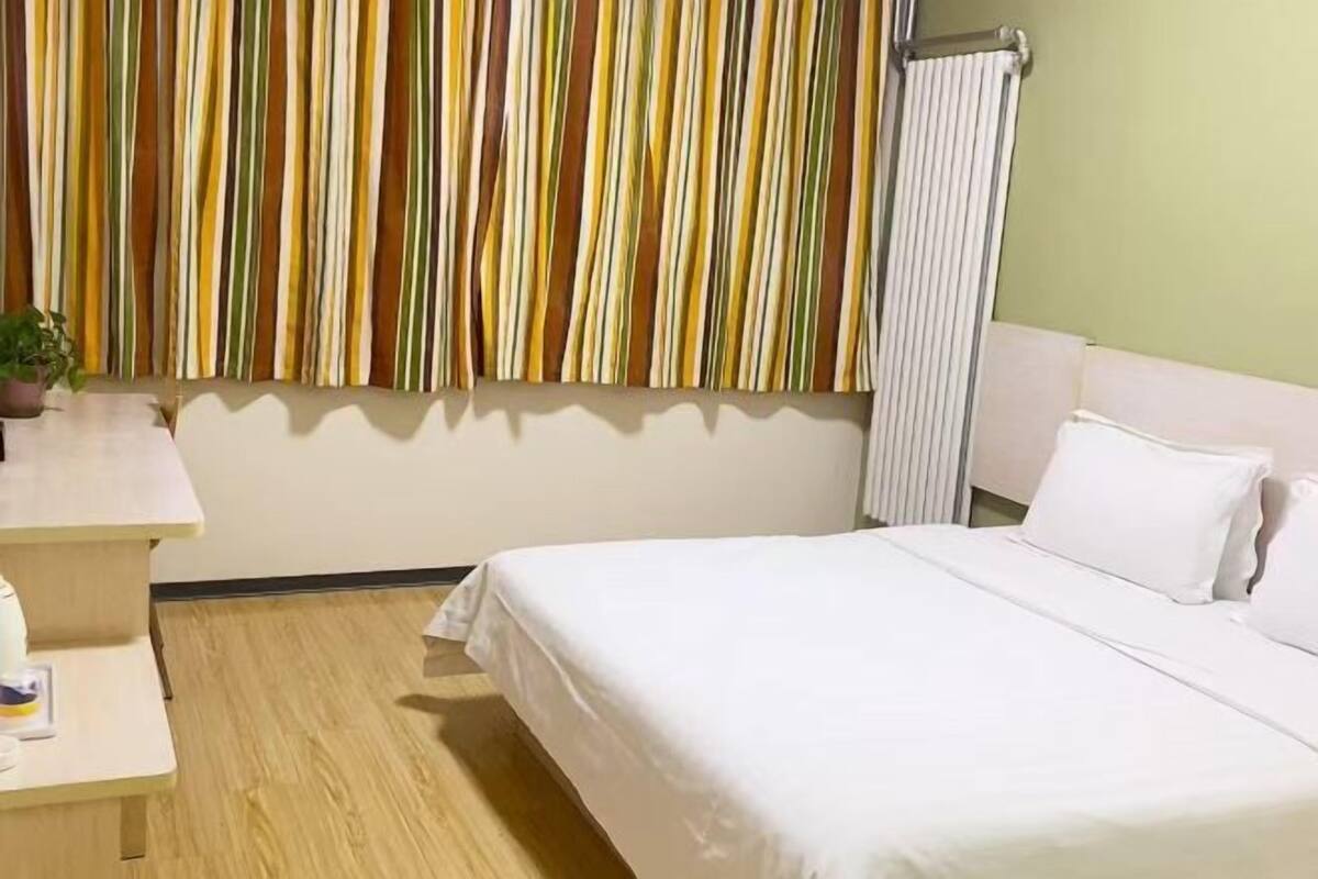 Quarto de hotel com uma cama, mesa de cabeceira, radiador e cortina listrada.