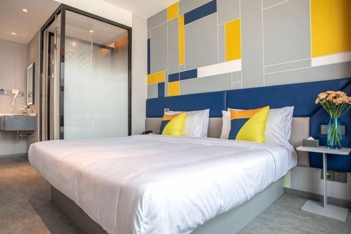 Quarto de hotel com uma cama grande, uma mesa de cabeceira, um espelho e um design moderno na parede.