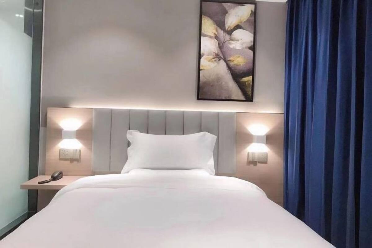 Quarto de hotel com uma cama, duas luminárias de cabeceira, um telefone e um quadro na parede.