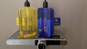 Dos botellas de champú y acondicionador sobre una repisa con un regulador de temperatura.