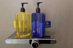 Hyllyllä on kaksi pulloa shampoota ja hoitoainetta, ja hyllyn vieressä on lämpötilansäätönuppi.