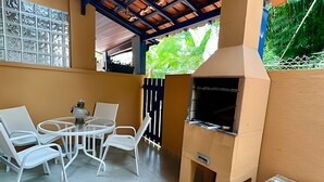 Une terrasse extérieure avec un barbecue, des chaises en métal blanches et une table.