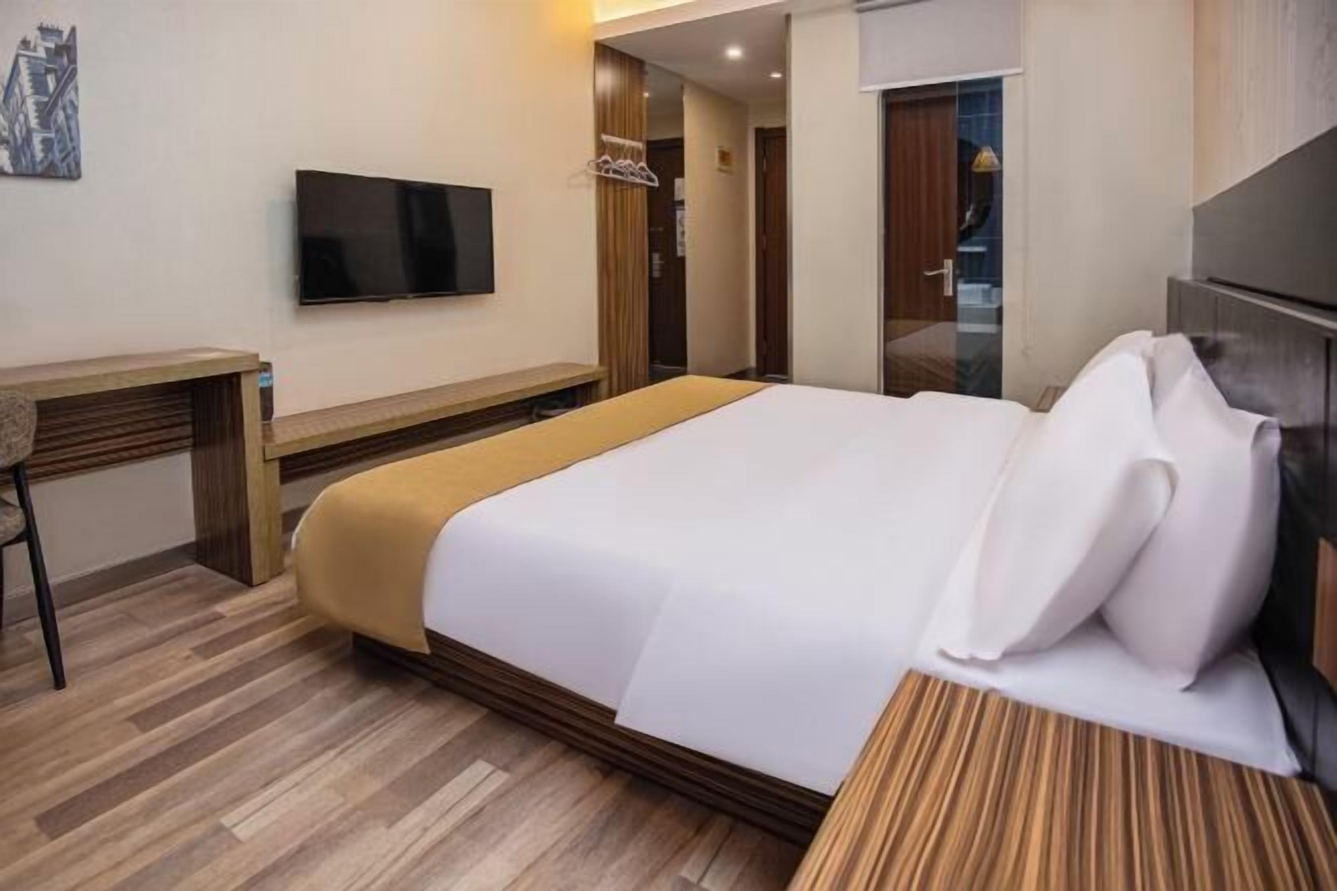 A hotel room with a bed, a desk, a television, and a wardrobe.