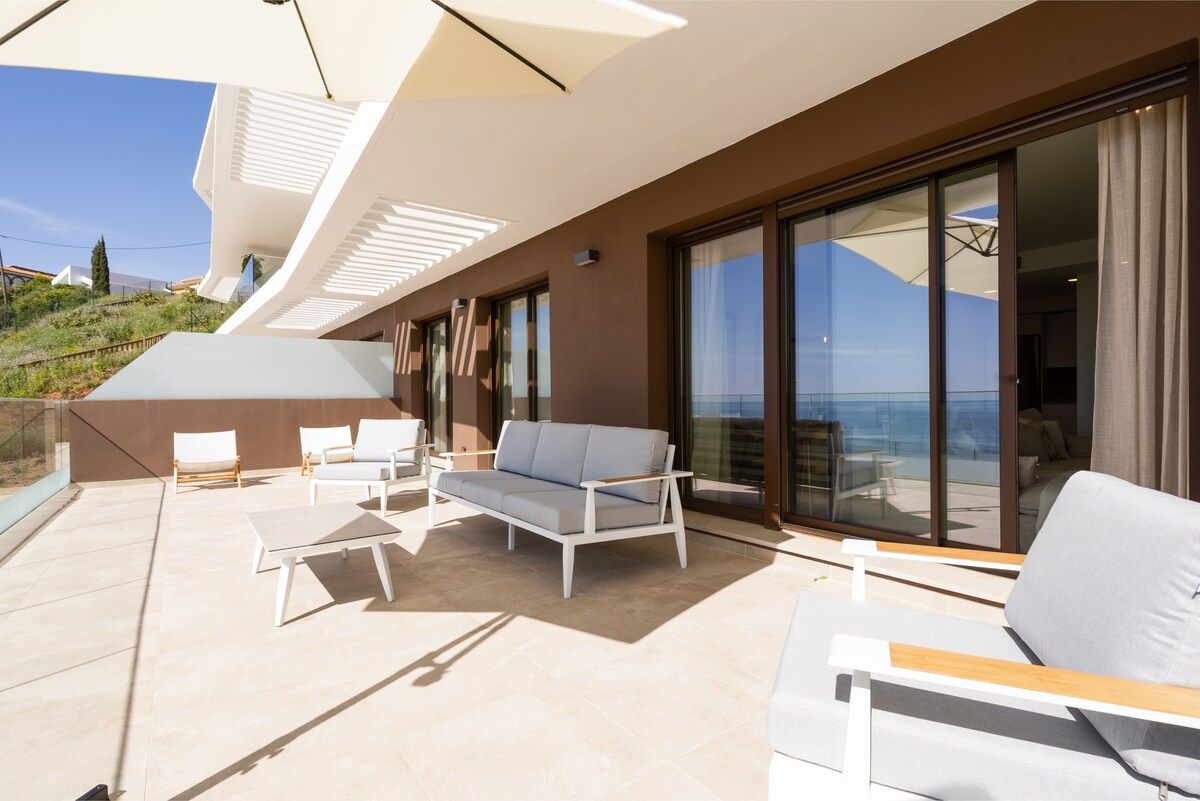 A modern outdoor living area with a sofa, chairs, and a table, overlooking a scenic view.