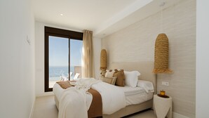 Een slaapkamer met een groot bed, een klein nachtkastje, uitzicht op zee en een plafondlamp.