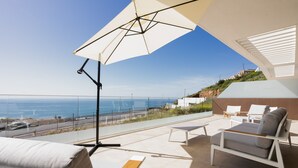 Een balkon met uitzicht op zee, een witte parasol en tuinmeubilair.