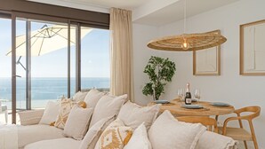 Een moderne woonkamer met een groot raam, een bank met opvallende kussens, een eettafel met stoelen en een hanglamp.