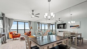 Ein modernes Wohnzimmer mit Essbereich, großen Fenstern, Deckenventilatoren und einem Flachbildfernseher.