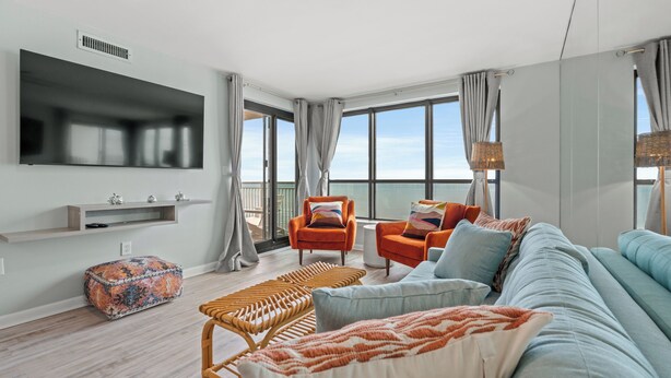 Ein modernes Wohnzimmer mit einer großen Couch, zwei Sesseln, einem Couchtisch und einem an der Wand montierten Fernseher.