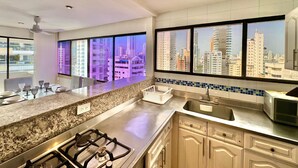 Une cuisine moderne équipée d’une cuisinière à gaz, d’un four à micro-ondes et d’une grande fenêtre donnant sur la ville.