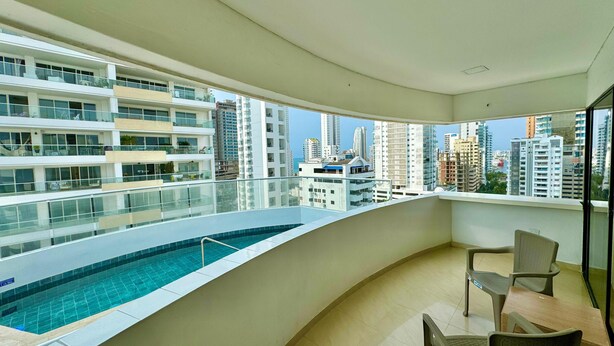 Un appartement moderne doté d’un balcon donnant sur une piscine et des immeubles de grande hauteur.