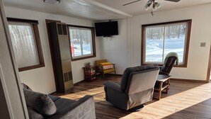 Un salon avec un canapé, un fauteuil et un téléviseur fixé au mur.