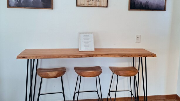 Une table en bois, trois tabourets, des tableaux encadrés accrochés au mur et une enseigne sur laquelle on peut lire : « Le lieu de rencontre ».