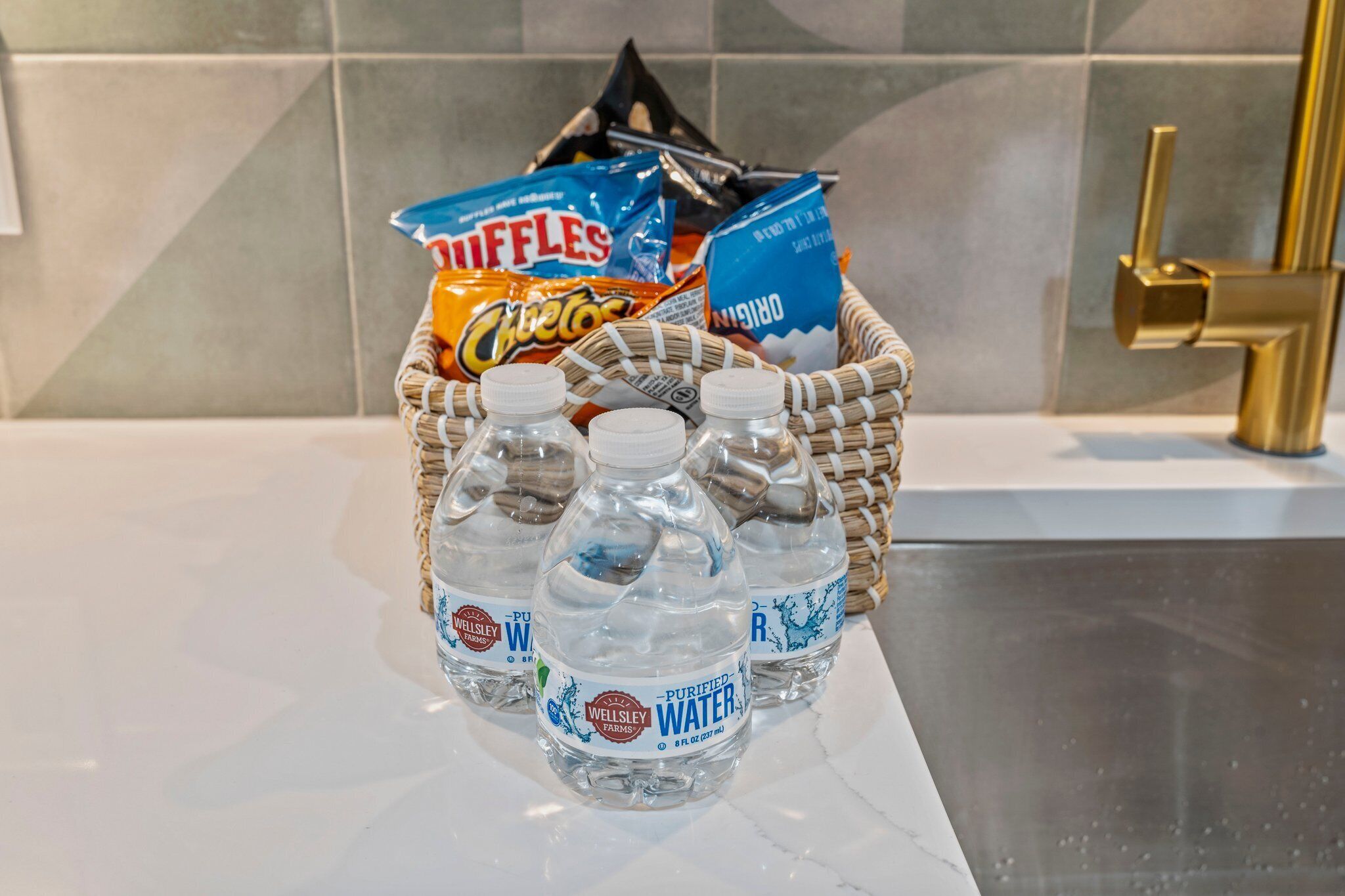 Una encimera de cocina con una cesta que contiene botellas de agua, una bolsa de papas fritas y una caja de gofres.