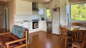 Eine moderne Küche mit weißen Schränken, einer Mikrowelle und einem Kühlschrank. Ein Esstisch mit Stühlen bietet Blick auf Grünflächen.