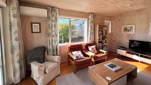 Ein Wohnzimmer mit einer Couch, zwei Sesseln, einem Couchtisch, einem Fernseher und einem Bücherregal.