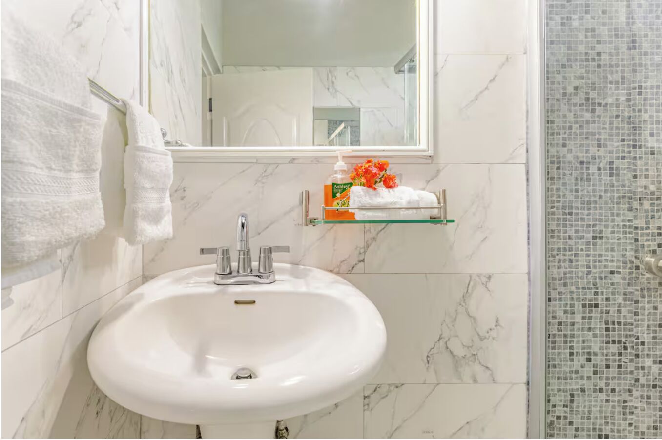 A bathroom with a white sink, a mirror, and a shower area with mosaic tiles.