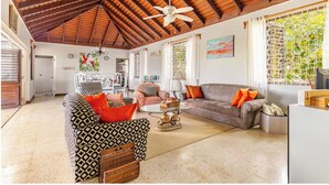 A spacious living area with a high ceiling, a ceiling fan, and a large window with a view of greenery. - Charming 3-bedroom villa in enchanting Trelawny with AC, WiFi (Trelawny)