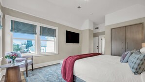 A bedroom with a large bed, a chair, a small table, a TV, and a wardrobe.