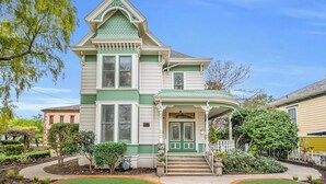 A two-story Victorian-style house with a green and white facade, a front porch, and a well-maintained garden.