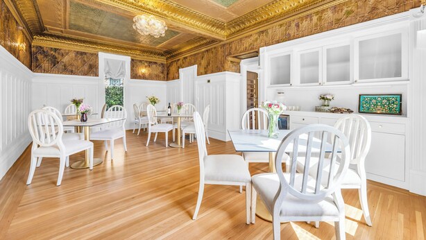 A dining room with white chairs, a glass table, and a chandelier.