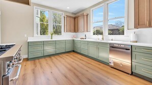 A modern kitchen with green cabinets, a stainless steel range, and a dishwasher.