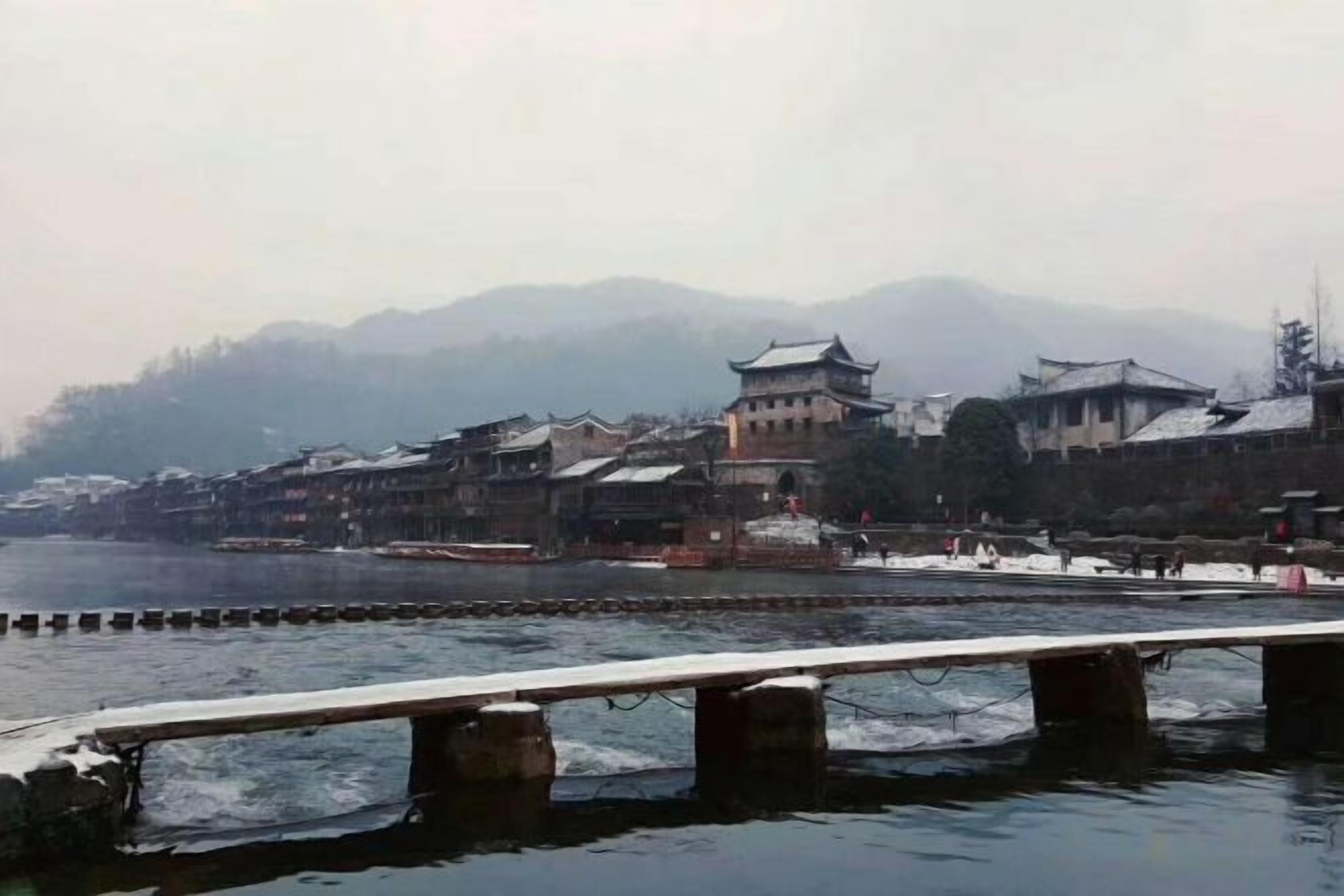 A riverside view with traditional buildings, a bridge, and a mountain backdrop.