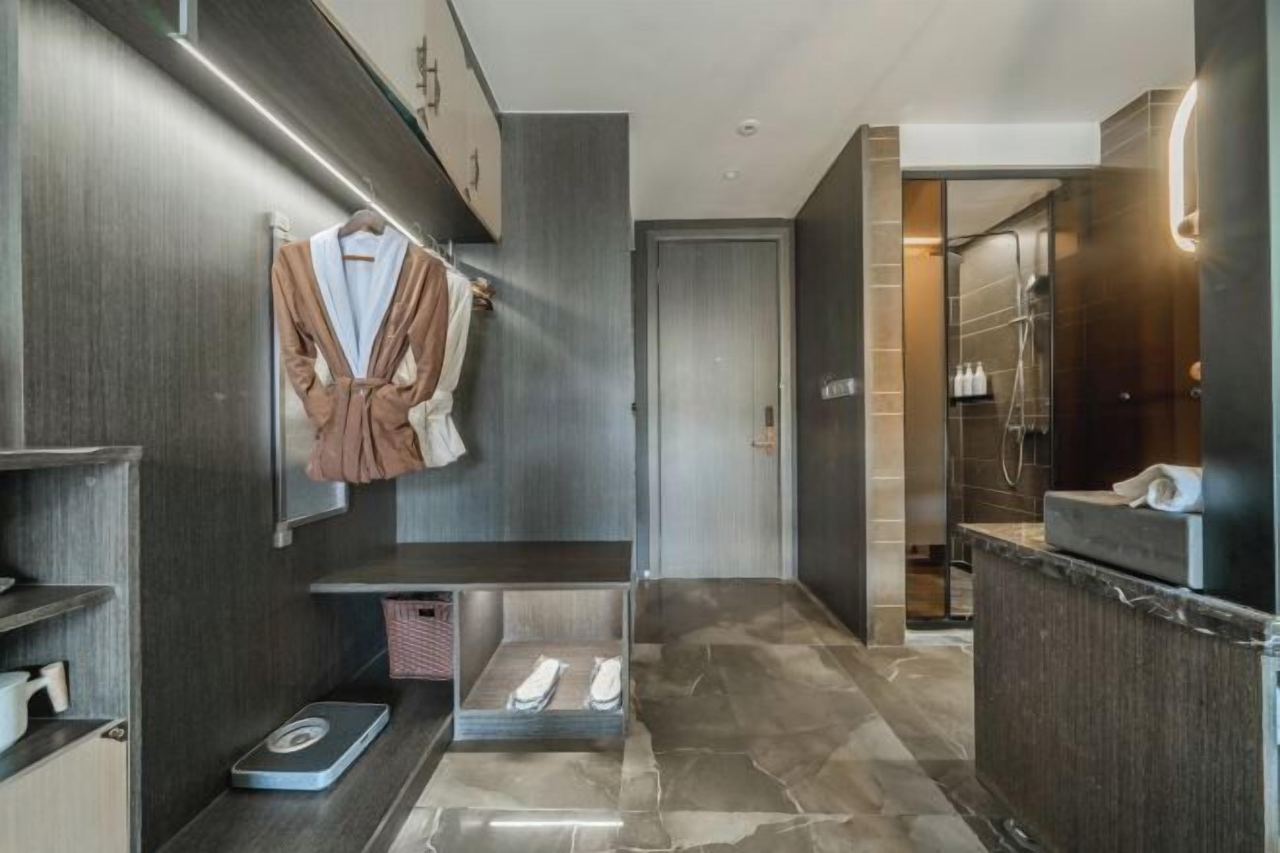 A modern bathroom with a marble floor, a towel rack with robes, a scale, and a shower area.