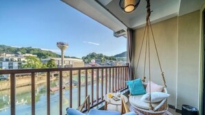 A balcony with a hanging chair, a small table with a glass of orange juice, and a view of a river and buildings. - Dengnilai Inn (Fenghuang County)