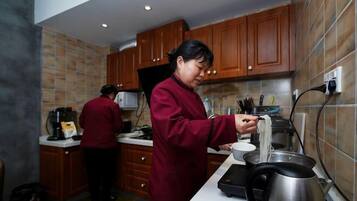 A kitchen with wooden cabinets, a countertop, a kettle, and a person preparing food.