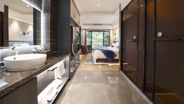A modern hotel room with a large bathroom vanity, a bed with a blue accent, and a view of the outdoors through large windows. - Dengnilai Inn (Fenghuang County)