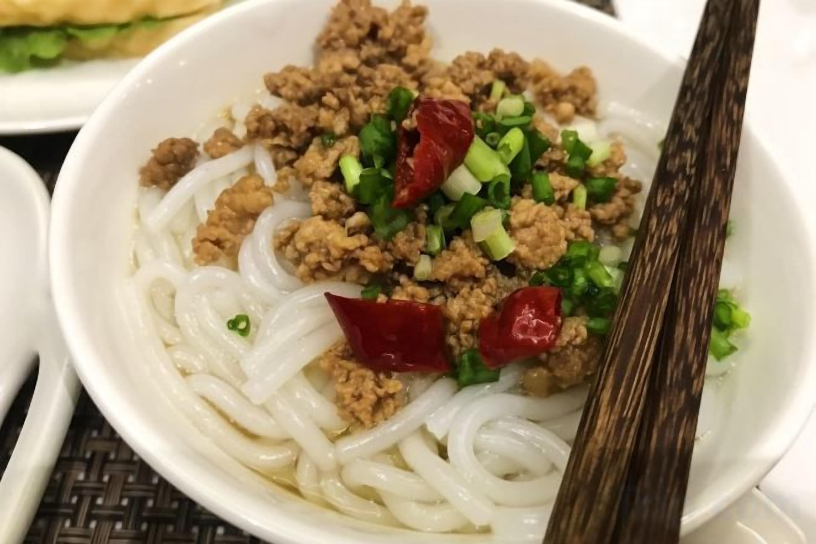 Un bol de soupe de nouilles avec de la viande hachée et des oignons verts.