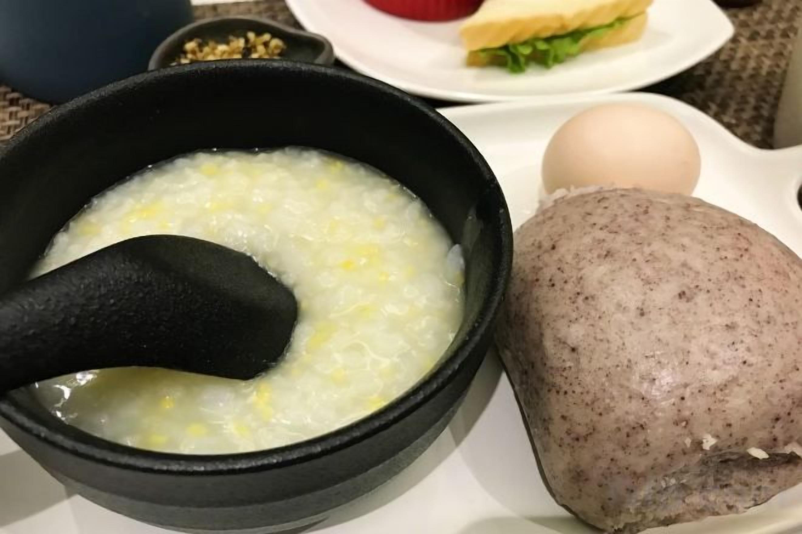 A bowl of porridge with a spoon, a boiled egg, and a round meat dish on a plate.
