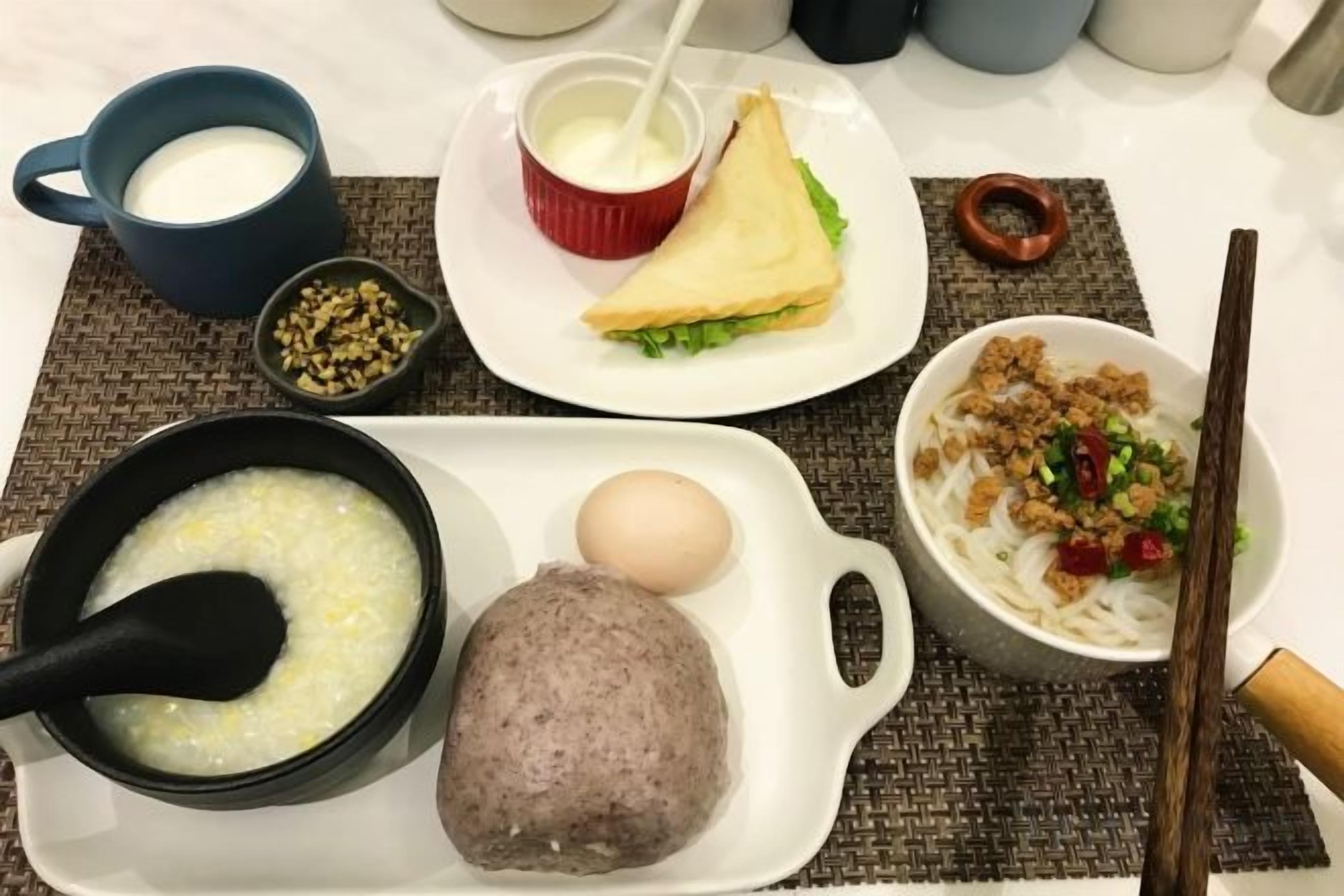 A meal with various dishes including a bowl of soup, a plate with a sandwich, a bowl of noodles, and a plate with a meat patty.