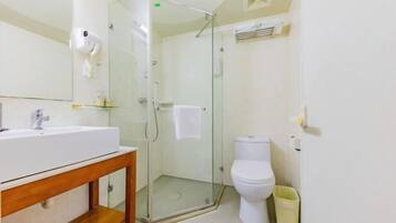 Un baño con ducha de vidrio, lavamanos blanco y retrete.