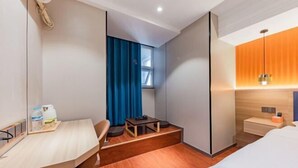 Ein modernes Hotelzimmer mit Holzboden, einem Schreibtisch mit Stuhl, einem Bett, einem kleinen Tisch und einem Fenster mit blauen Vorhängen.