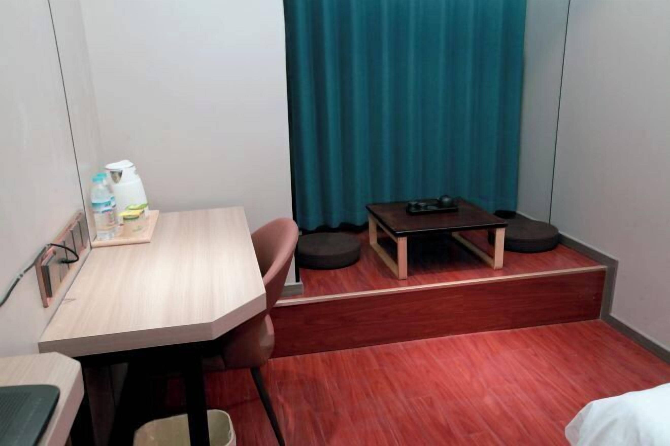 Une chambre d’hôtel compacte, dotée d’un bureau en bois, d’une chaise, d’une petite table avec une télécommande et d’un rideau de couleur turquoise.