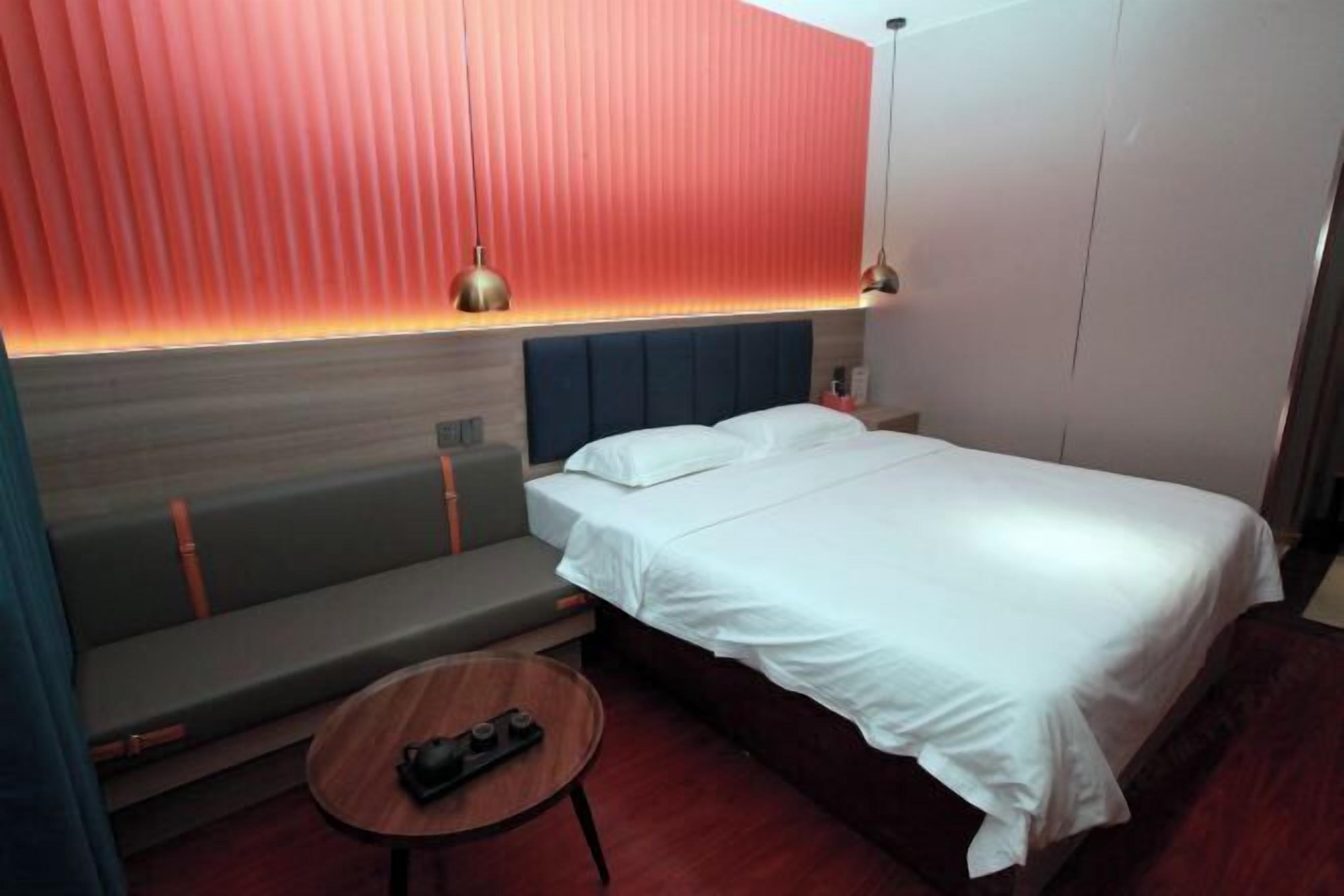 Een hotelkamer met een bed, een bankje, een klein tafeltje en een muur met verticale latten.